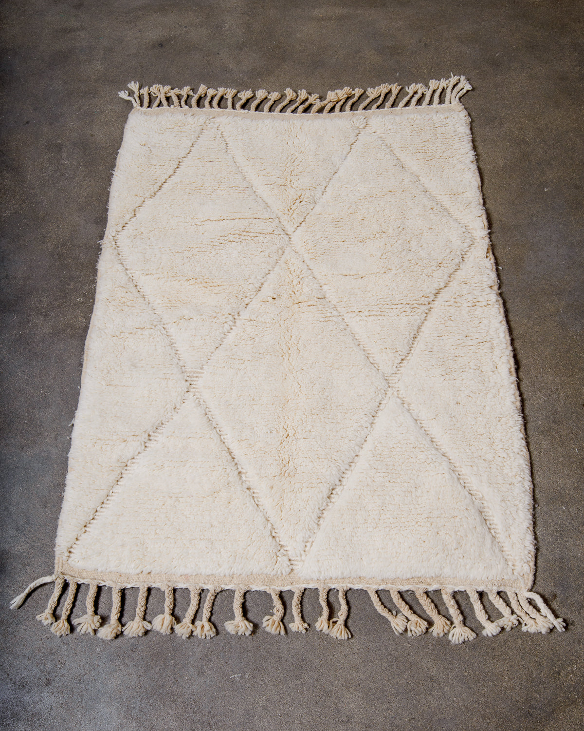 Beniourain rug in cream wool laying on concrete studio floor.